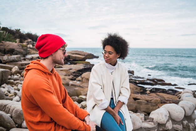 Retrato de dois jovens amigos a passar bons momentos juntos e a ter uma conversa enquanto está sentado com o mar no espaço.