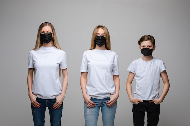 Retrato de duas garotas bonitas com cabelo longo loiro e um jovem com máscaras médicas pretas em seus rostos isolados em um fundo cinza