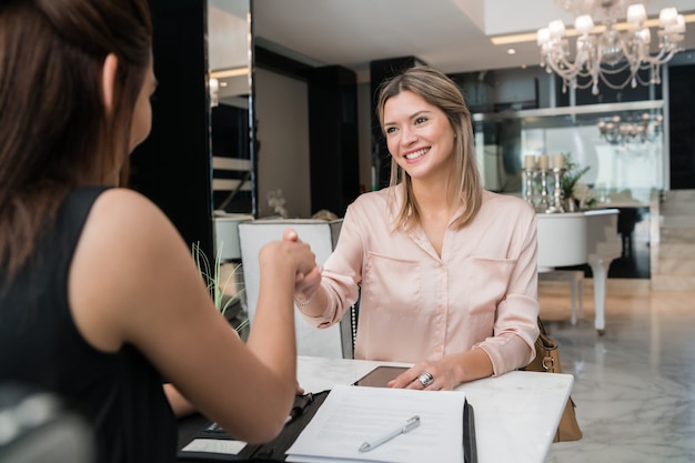 Foto grátis retrato de duas jovens empresárias tendo reunião e aperto de mãos no saguão do hotel. conceito de viagens de negócios.