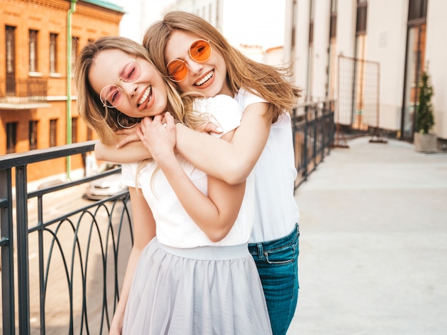 Retrato de duas meninas de hipster loira sorridente jovem bonita em roupas de camiseta branca na moda verão. . modelos positivos se divertindo em óculos de sol.