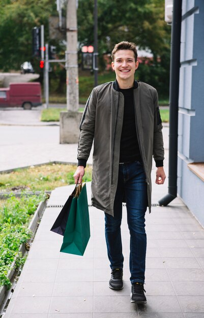 Retrato, de, elegante, homem jovem, andar, com, bolsas para compras, em, ao ar livre