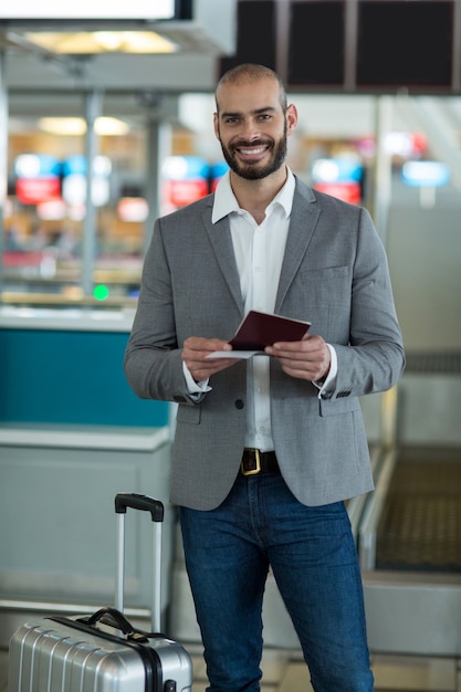 Retrato de empresário sorridente com bagagem verificando seu cartão de embarque