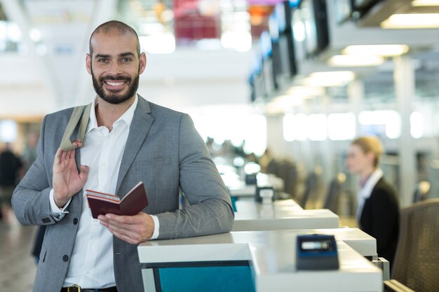 Retrato de empresário sorridente em pé no balcão de check-in com passaporte e cartão de embarque