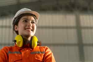 Foto grátis retrato de engenheira asiática vestindo uniforme e capacete de segurança em pé confiante e alegre ao lado da máquina de braço robô de automação no fundo da fábrica