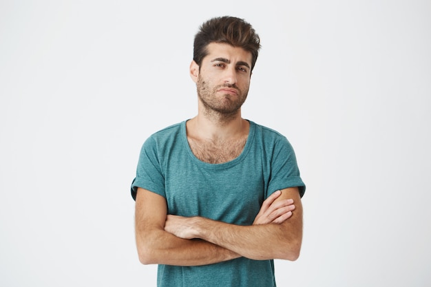 Retrato de espanhol atraente jovem confiante em camiseta azul e corte de cabelo à moda, cruzando as mãos, sendo super ciumento vendo ex namorada com novo homem.