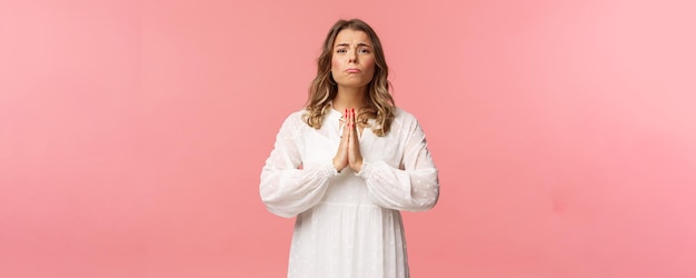 Retrato de esperançosa namorada grudenta menina loira implorando por favor em vestido branco sobre fundo rosa soluçando faz olhos bonitos implorando ou rezando diga por favor quer algo mal