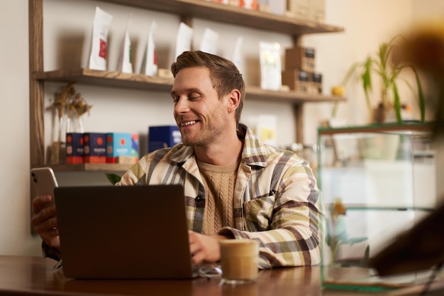 Foto grátis retrato de estilo de vida de um jovem empresário freelancer sentado em um café bebendo café e usando um laptop