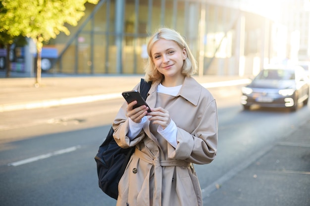 Retrato de estilo de vida de uma jovem na rua de pé perto da estrada com carros carregando mochila e segurando