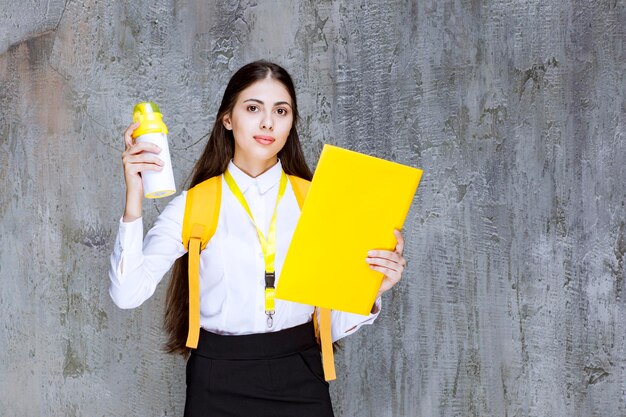 Retrato de estudante bonita segurando a garrafa de água amarela e notebook. Foto de alta qualidade