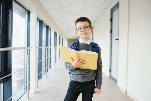 Retrato de estudante de escola feliz óculos de criança inteligente da escola primária em pé na escola criança segurando um livro
