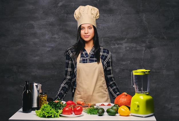 Retrato de estúdio de cozinheiro feminino chef à mesa com um monte de legumes.