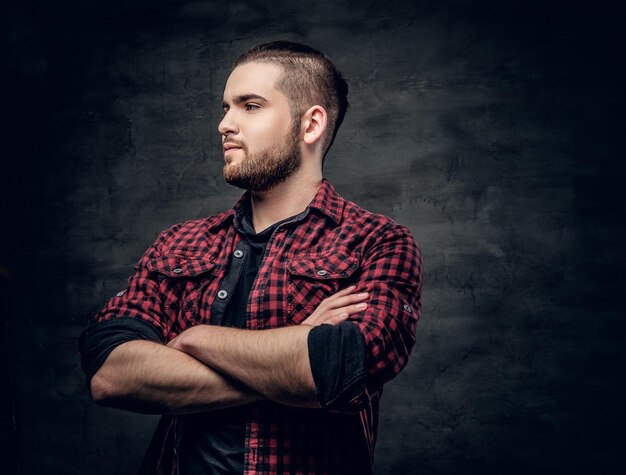 Retrato de estúdio de homem hipster barbudo com braços cruzados, vestido com uma camisa de lã vermelha sobre fundo cinza.