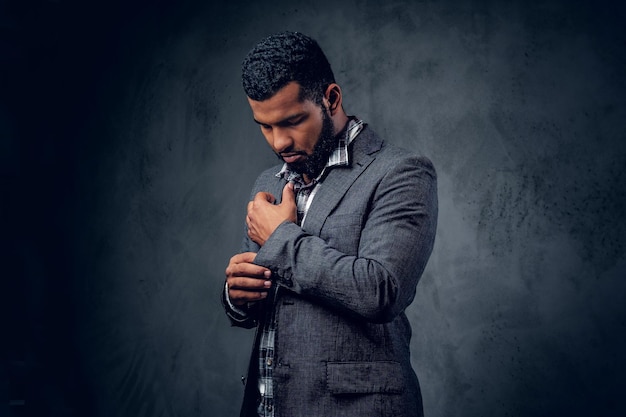 Retrato de estúdio de homem hipster preto vestido com uma camisa de lã e uma jaqueta posando sobre fundo artístico cinza.