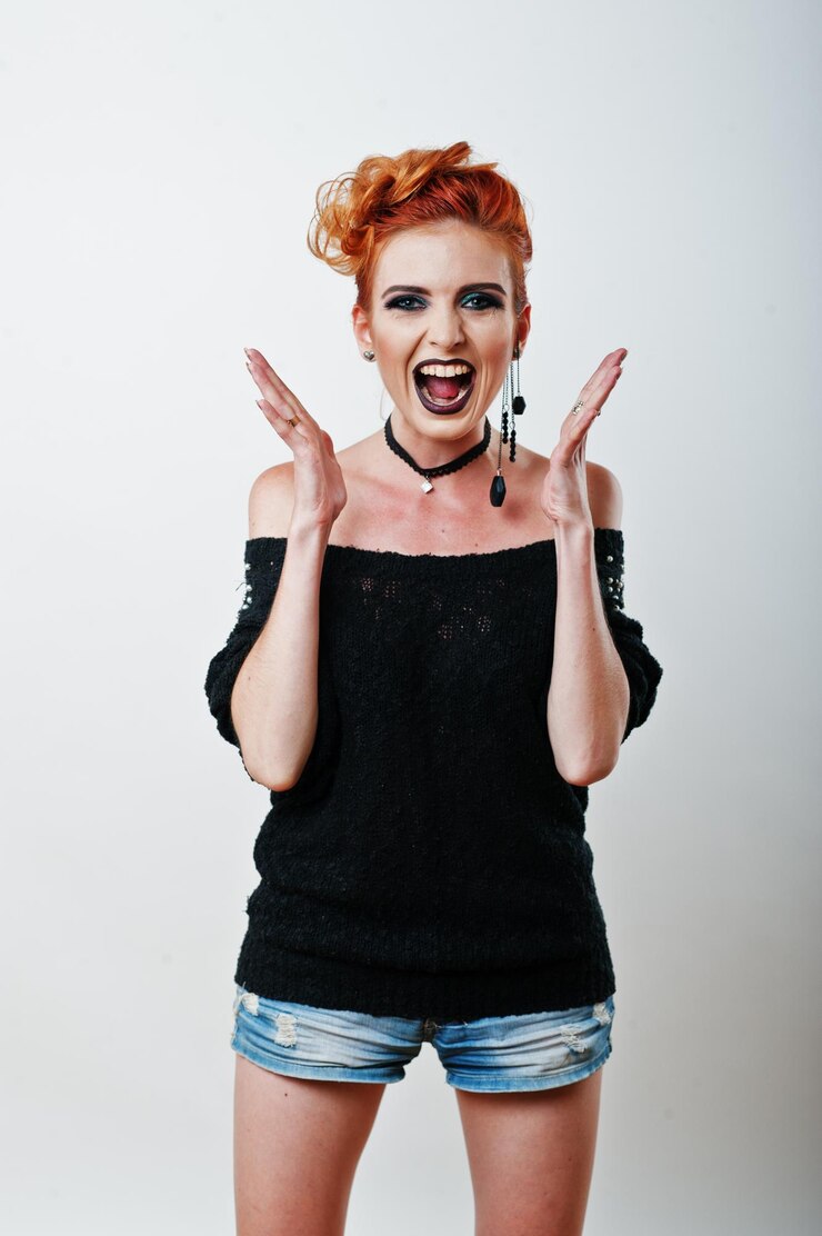Foto grátis retrato de estúdio de menina de cabelos vermelha na blusa preta e shorts jeans com maquiagem escura brilhante