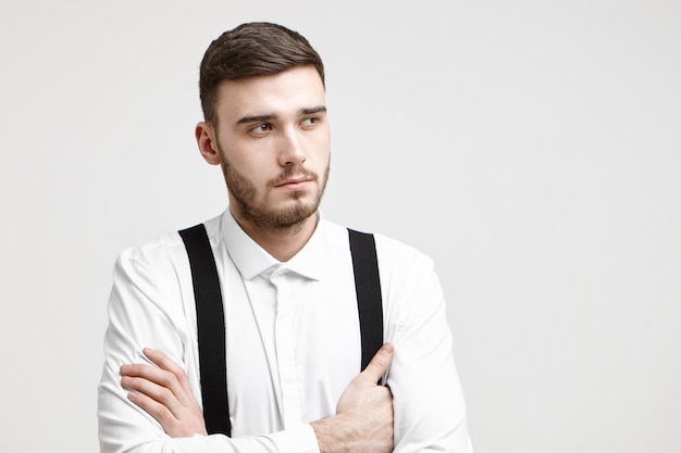 Retrato de estúdio de um empresário jovem e bonito com a barba por fazer em traje formal, mantendo os braços cruzados enquanto pensa em conceitos, ideias, soluções, estratégias e perspectivas relativas a seu novo projeto de negócios