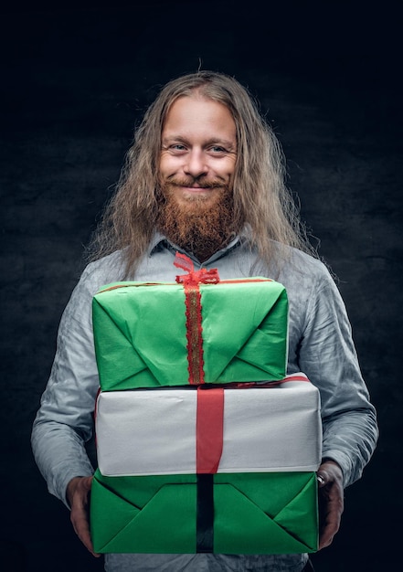 Retrato de estúdio de um homem barbudo positivo com cabelo comprido detém as caixas presentes.