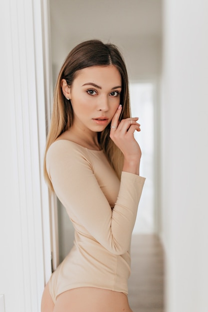 Retrato de estúdio interno do modelo muito natural, vestindo o corpo bege, posando para a câmera. Senhora adorável e alegre posando em seu apartamento