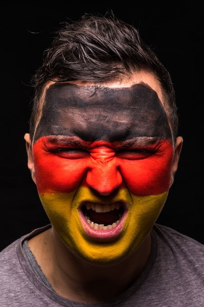 Retrato de fã de torcedor de rosto de homem bonito da seleção da alemanha com a cara da bandeira pintada isolada no fundo preto. emoções dos fãs.