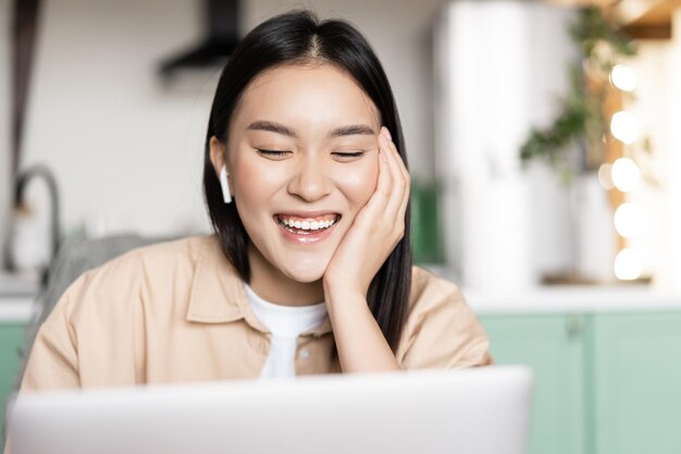 Retrato de feliz menina asiática fala no bate-papo por vídeo, comunicando-se com o aplicativo de laptop rindo e.