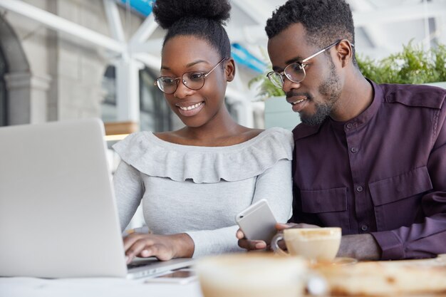 Retrato de felizes alunos de pele escura se reúnem para fazer apresentações ou projetos, sentar no refeitório, pesquisar informações na internet por meio de um laptop portátil.