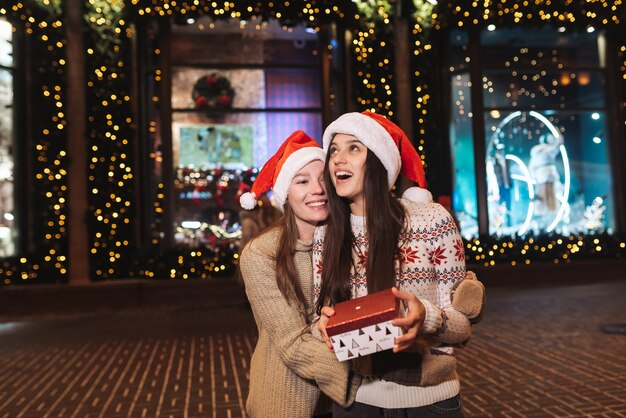 Retrato de felizes fofos jovens amigos abraçando uns aos outros e sorrindo enquanto caminhava ao ar livre na véspera de Natal.