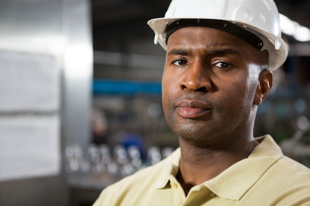 Retrato de funcionário sério do sexo masculino usando capacete na fábrica