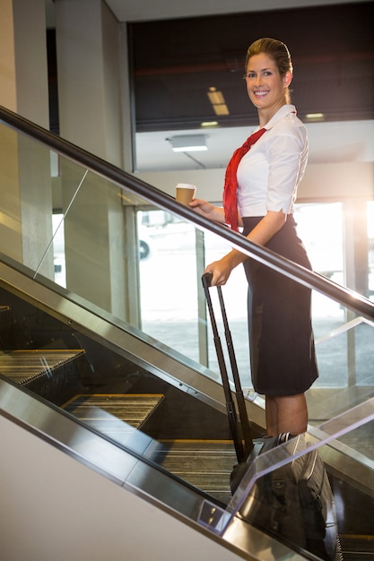 Retrato de funcionários do sexo feminino com bagagem na escada rolante
