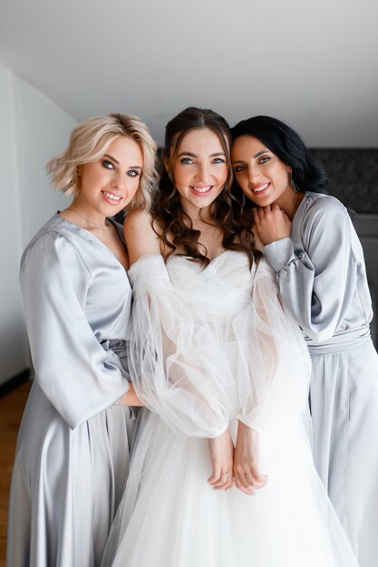 Retrato de grupo de damas de honra com noiva elegante em vestido inchado em pé na sala olhando para a câmera se preparando para a cerimônia do dia do casamento com emoções positivas