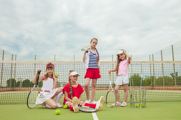 Retrato de grupo de garotas como tenistas segurando a raquete de tênis contra a grama verde da quadra ao ar livre