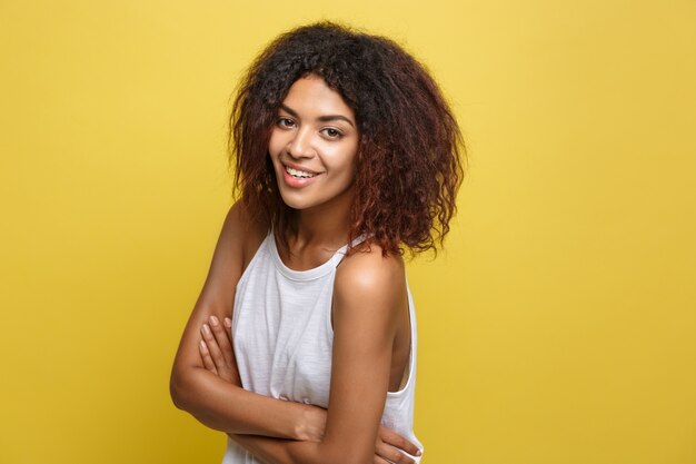 Retrato de Headshot da bela e atrativa mulher afro-americana posta os braços cruzados com o sorriso feliz. Fundo de estúdio amarelo. Espaço de cópia.
