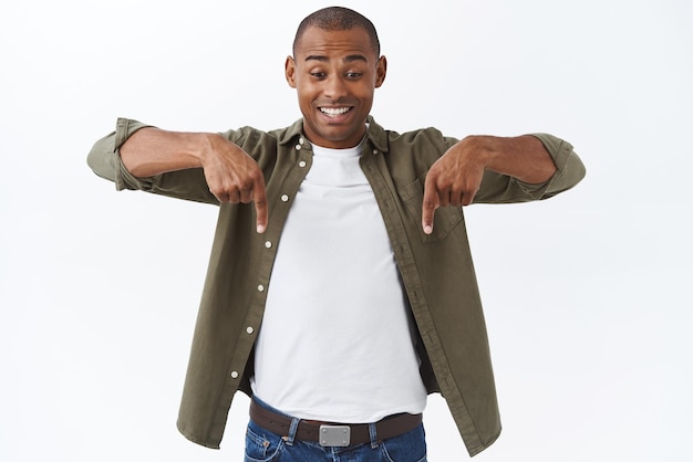 Retrato de homem afro-americano alegre animado feliz homem apontando para baixo vendo uma boa oferta desconto especial finalmente encontrou um bom negócio em pé fundo branco espantado