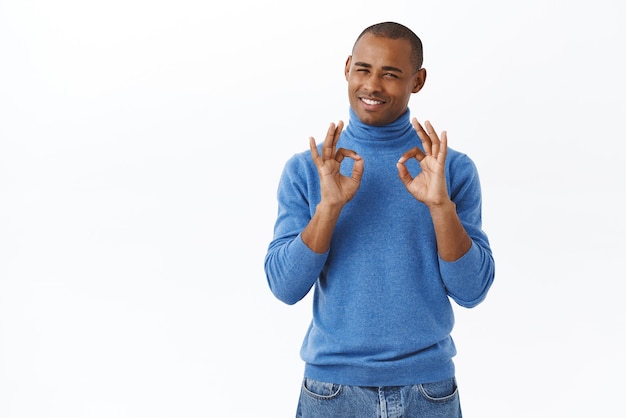 Retrato de homem afro-americano bonito satisfeito mostrando sinal de ok garante melhor qualidade sendo satisfeito com serviço perfeito descrevendo incrível viagem de férias para resort fundo branco