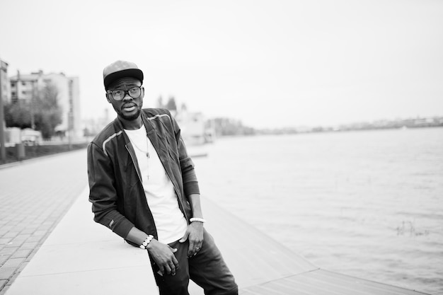 Retrato de homem afro-americano estiloso em boné esportivo e óculos contra o lago black men model fashion