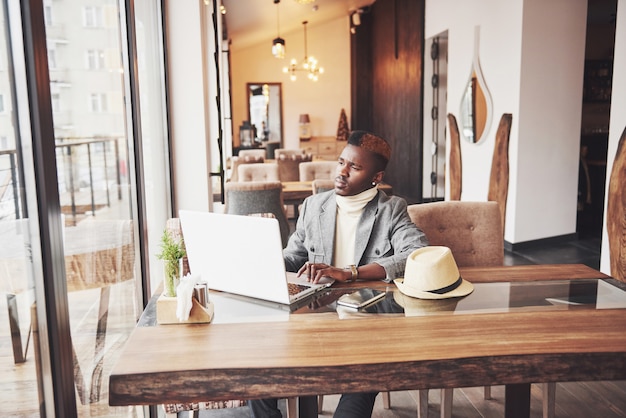 Retrato de homem afro-americano sentado em um café e trabalhando em um laptop