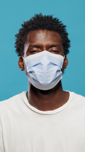 Retrato de homem afro-americano, usando máscara facial para proteger contra coronavírus em estúdio. Perto da pessoa negra, olhando para a câmera, tendo a máscara protetora no rosto sobre o fundo.