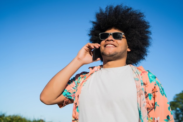 Retrato de homem afro-latino falando ao telefone em pé ao ar livre na rua