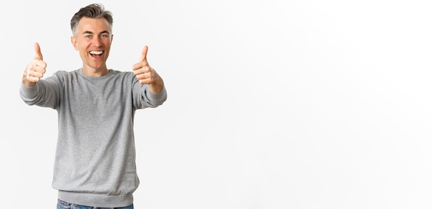 Foto grátis retrato de homem alegre de meia-idade elogiando o bom trabalho em pé sobre fundo branco mostrando os polegares
