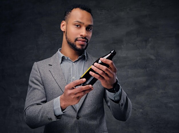 Retrato de homem americano preto elegante vestido com um terno cinza segura uma garrafa de cerveja artesanal.