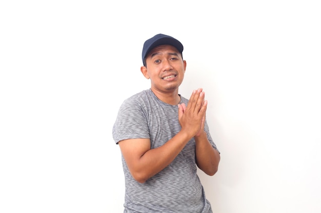 Retrato de homem asiático com camiseta cinza e chapéu azul implora perdão por seu erro