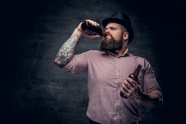 Retrato de homem barbudo em uma camisa xadrez e um chapéu de cilindro, bebendo cerveja de uma garrafa.