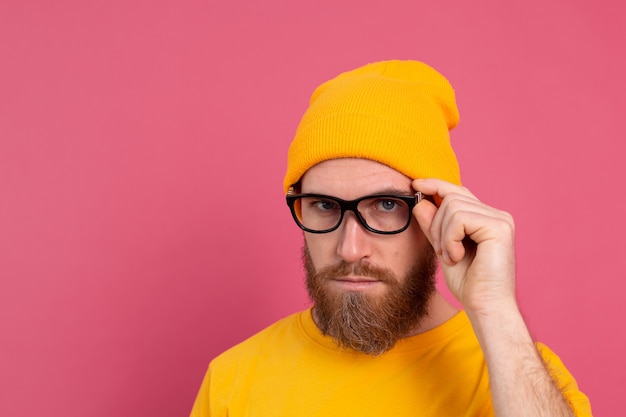 Retrato de homem barbudo europeu bonito elegante com chapéu de camisa amarela casual e óculos rosa