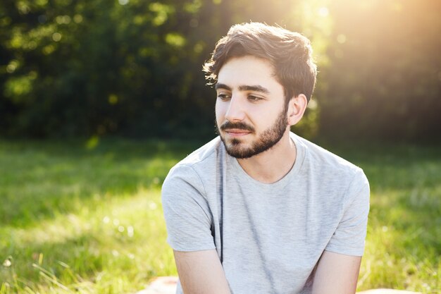 Retrato de homem barbudo pensativo com penteado elegante, olhando para baixo com seus encantadores grandes olhos escuros, pensando sobre sua vida, desfrutando de quietude