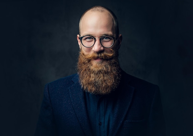 Retrato de homem barbudo ruiva em óculos vestido com um terno de lã elegante sobre fundo cinza.