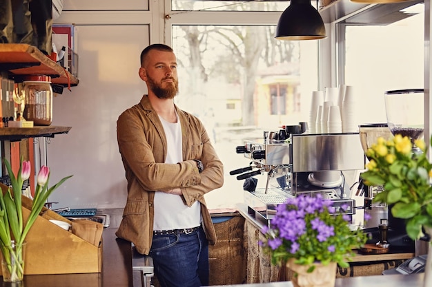 Retrato de homem barbudo ruivo em um pequeno café com muitas flores e máquina de café.