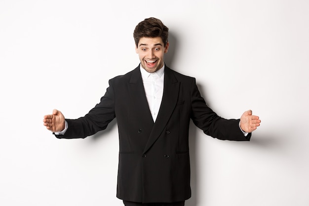 Retrato de homem bonito animado de terno, moldando grande objeto no espaço da cópia e sorrindo espantado, segurando algo, de pé sobre um fundo branco.