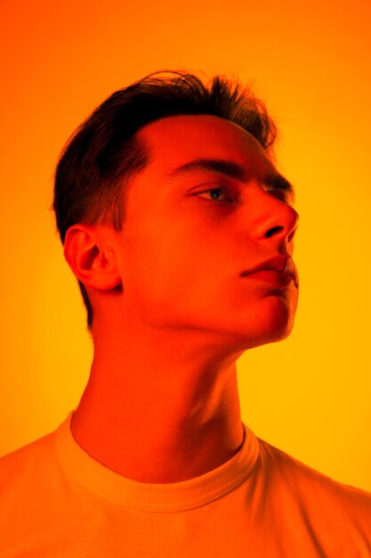Retrato de homem bonito caucasiano isolado no fundo laranja do estúdio em luz de néon, monocromático. Lindo modelo masculino. Conceito de emoções humanas, expressão facial, vendas, publicidade, moda e beleza.