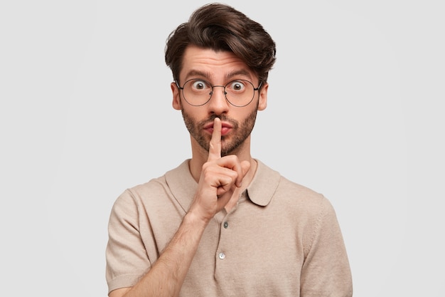 Retrato de homem bonito com a barba por fazer mantendo o dedo da frente nos lábios