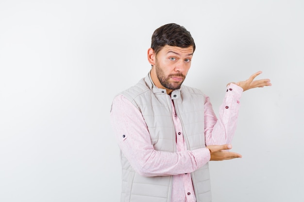 Retrato de homem bonito fingindo mostrar algo no colete, camisa e parecendo confiante