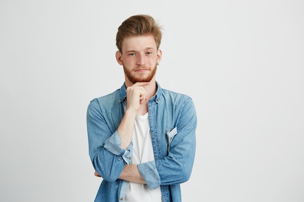 Retrato de homem bonito jovem confiante com barba pensando com mão no queixo.