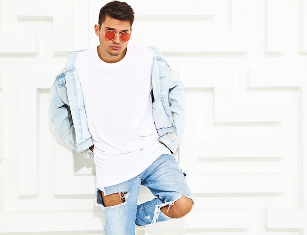 Retrato de homem bonito jovem modelo vestido com roupas jeans posando perto de parede texturizada branca